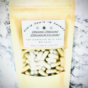 May include: A beige pouch with a clear window displaying numerous white capsules. The label reads "Liv's Tea's 'N Things" and "Organic Oregano (Origanum Vulgare)". It contains 120 capsules with 400+ mg each, with a best-by date of June 2027.