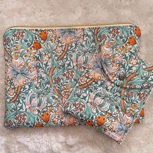 May include: A floral pattern clutch and matching accessory. The fabric features a repeating design of orange lilies, teal leaves, and small red flowers on a white background. The clutch has a gold zipper.
