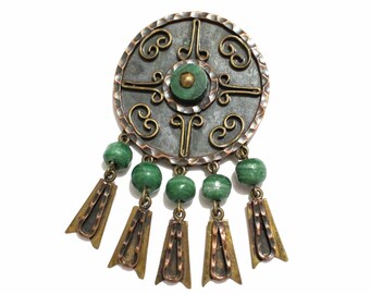 May include: A circular copper and brass brooch with a green malachite stone in the center. The brooch has a decorative design with a filigree pattern and is accented with green malachite beads.