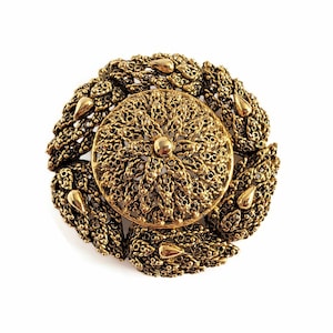 Op de afbeelding: Een gouden filigraan broche met een rond ontwerp. Het midden van de broche heeft een kleiner rond ontwerp met een verhoogd midden.