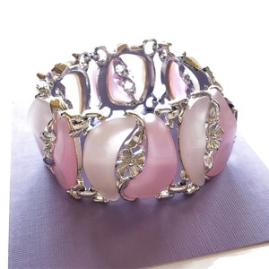 May include: A silver bracelet with pink and white oval-shaped stones. The stones are set in a silver floral design.