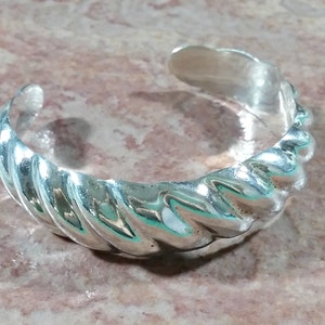 May include: A silver bracelet with a twisted design. The bracelet is made of smooth, polished metal and has a simple, elegant look.