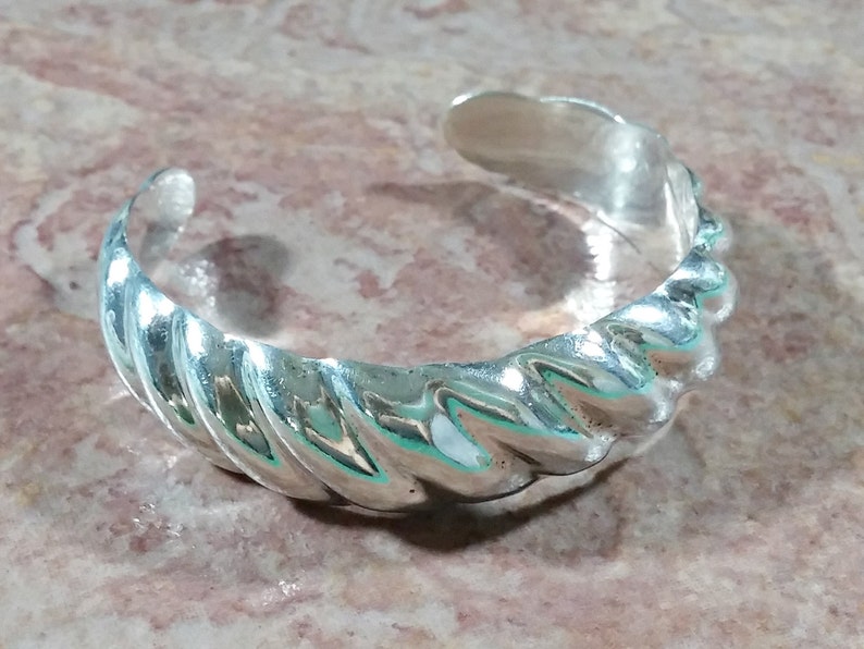 May include: A silver bracelet with a twisted design. The bracelet is made of smooth, polished metal and has a simple, elegant look.