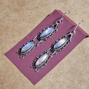 May include: A pair of silver earrings with iridescent opal stones. The earrings are long and dangle, with a delicate filigree design.