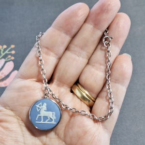 May include: A silver chain bracelet with a blue and white cameo pendant featuring the zodiac sign Sagittarius.