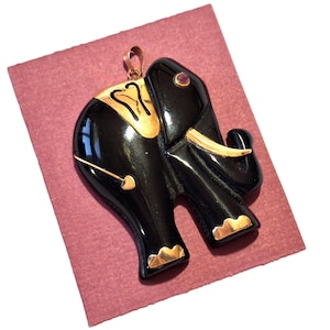 May include: A black onyx elephant pendant with gold accents and a red gemstone eye. The pendant is on a red velvet background.