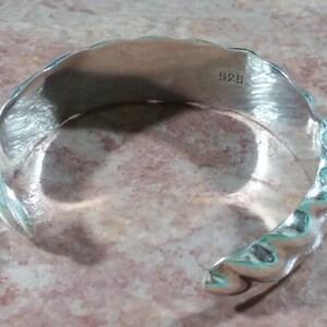 May include: Silver bracelet with a textured, wavy design. The bracelet is stamped with "925" on the inside.
