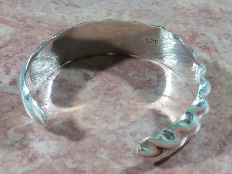 May include: Silver bracelet with a textured, wavy design. The bracelet is stamped with "925" on the inside.