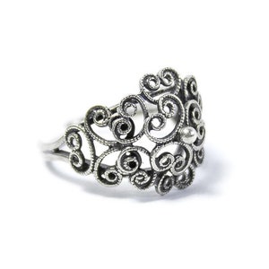 May include: A silver filigree ring with a delicate, intricate design. The ring is made of thin, twisted wire that forms a pattern of swirls and loops.