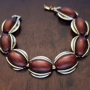 May include: A brown and silver bracelet with oval-shaped stones. The stones are a deep brown color and have a glossy finish. The bracelet is made of metal and has a simple design.