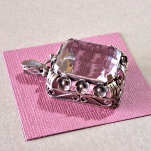 May include: A silver pendant with a large, clear, faceted gemstone set in a floral design. The pendant has a bail for attaching to a chain.