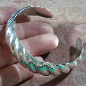 May include: A silver twisted bangle bracelet. The bracelet is made of a thick, twisted band of metal.