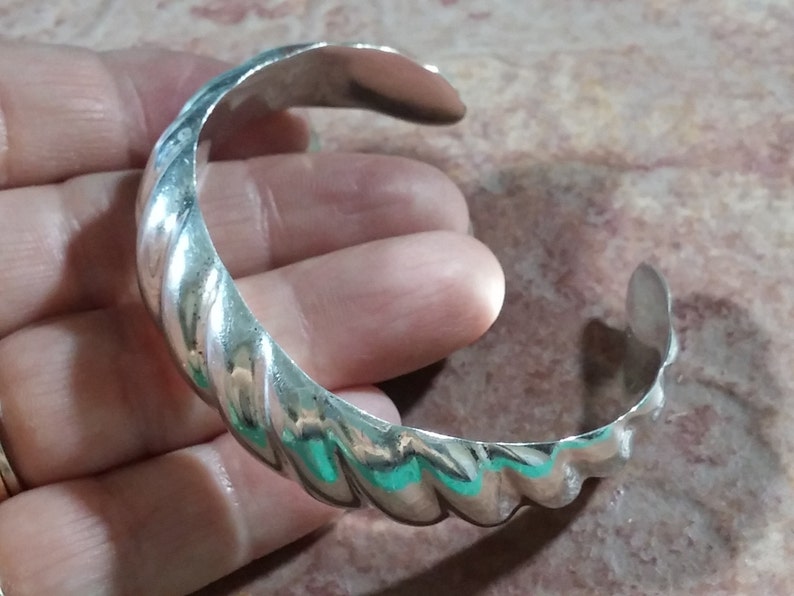 May include: A silver twisted bangle bracelet. The bracelet is made of a thick, twisted band of metal.