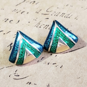May include: A pair of silver tone earrings with a geometric design. The earrings are triangular shaped and feature a green and blue enamel finish.