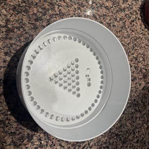 May include: A white plastic circular object with a series of small holes around the edge and a central design of a triangle made of small holes. The word "ZERO" is printed on the object.
