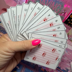 May include: A fan of white rectangular cards with black borders, each featuring a pink striped pattern and small red cherry illustrations. The cards are numbered from 1 to 12, with text on the reverse side including phrases like another save card.
