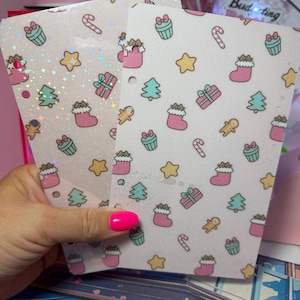 May include: Two rectangular planner inserts featuring a repeating holiday pattern of Pusheen cats in pink stockings, teal cupcakes, yellow stars, green Christmas trees, pink gift boxes, candy canes, and gingerbread men on a light pink background.