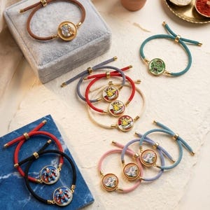 May include: A collection of adjustable cord bracelets featuring circular gold-toned metal charms with various colourful character illustrations. The bracelets come in diverse cord colours including brown, teal, red, white, black, pink, and blue.