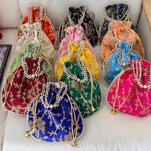 Può includere: Una collezione di borse colorate con coulisse e ricami floreali dorati. Ogni borsa presenta un manico con perline di perle e un nappa dorata. I colori includono rosso, nero, rosa, giallo, verde, blu e fucsia.