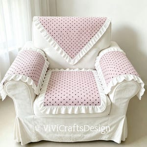 May include: A set of three light pink fabric covers for an armchair, featuring a pattern of small dark polka dots and white ruffled trim. The set includes a backrest cover, a seat cover, and two armrest covers, all with white ruffled edges.