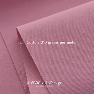 May include: Close-up of a soft, pink twill cotton fabric. The fabric has a subtle texture and is labeled "Twill Cotton 210 grams per meter".