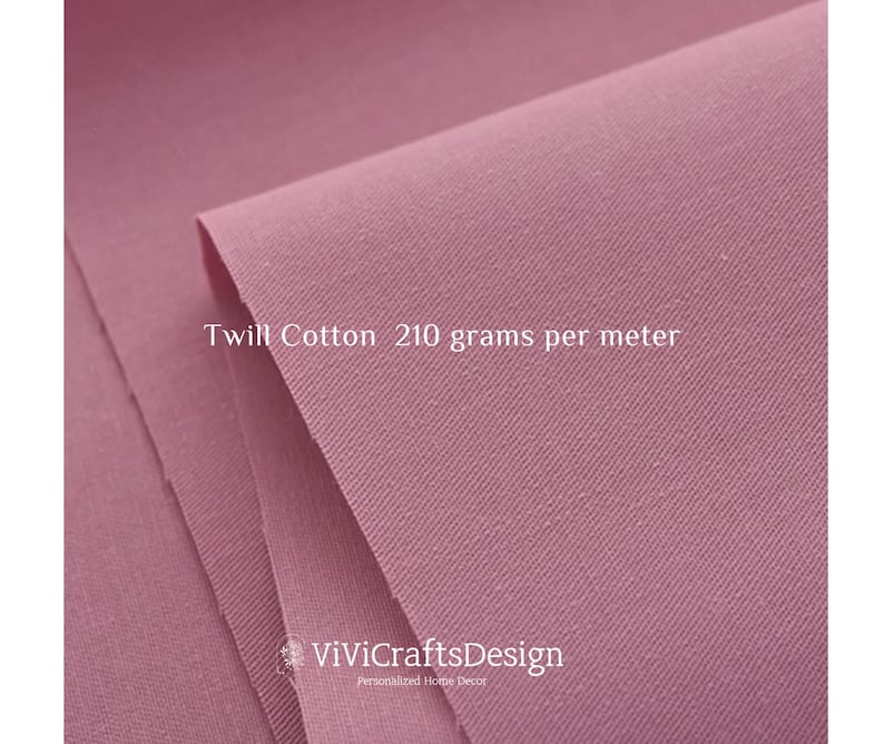 May include: Close-up of a soft, pink twill cotton fabric. The fabric has a subtle texture and is labeled "Twill Cotton 210 grams per meter".