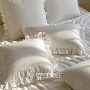 May include: White ruffled pillow covers with a white background. The pillow covers have a simple, elegant design and are perfect for adding a touch of sophistication to any bedroom.