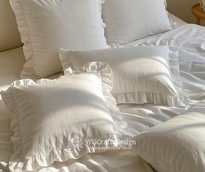 May include: White ruffled pillow covers with a white background. The pillow covers have a simple, elegant design and are perfect for adding a touch of sophistication to any bedroom.