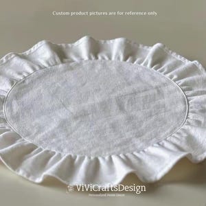 Op de afbeelding: Ronde, witte placemat met een gerimpelde rand. De placemat is gemaakt van een zachte, gestructureerde stof.