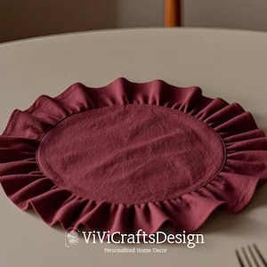 May include: A burgundy round placemat with a ruffled edge. The placemat is made of fabric and has a soft, textured surface.