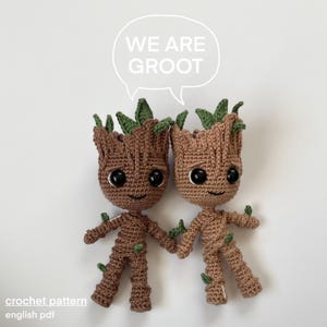 Peut inclure: Deux personnages Groot en crochet du film Les Gardiens de la Galaxie, debout côte à côte. Les personnages sont bruns avec des feuilles vertes et des yeux noirs. Le texte "We are Groot" est écrit dans une bulle de dialogue au-dessus des personnages.