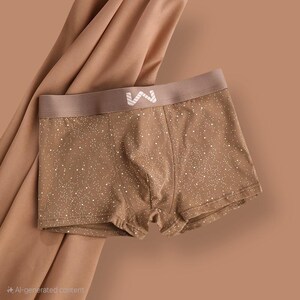 May include: Brown boxer shorts with a white speckled pattern and a brown waistband. The waistband features a white logo. The shorts are made of a soft material and are displayed against a brown background.