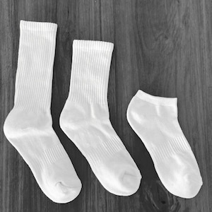 Puede incluir: Tres pares de calcetines blancos de diferentes tamaños. Los calcetines son de algodón y tienen una textura acanalada.