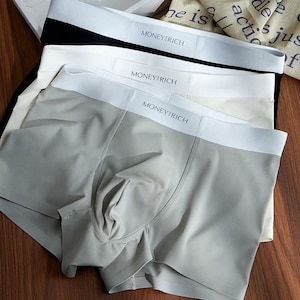 May include: A set of three boxer briefs in grey, white, and black. Each pair features a wide white elastic waistband with the text MONEY RICH printed in black. The fabric appears smooth and lightweight, with a contoured front pouch design.