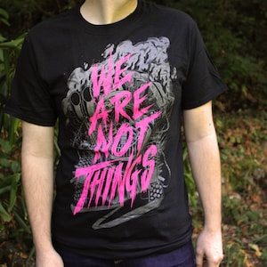 May include: Black t-shirt with a graphic print of a robot and the text "We Are Not Things" in pink.