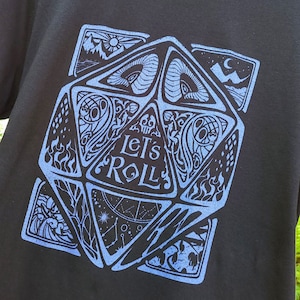May include: Black t-shirt featuring a blue graphic of a stylised dice with the text "Let's Roll" on it.