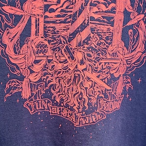 A closeup of the bottom of the red pirate shirt shows a pirate skull with a sword through it's eye and the text: fun at sea with friends.