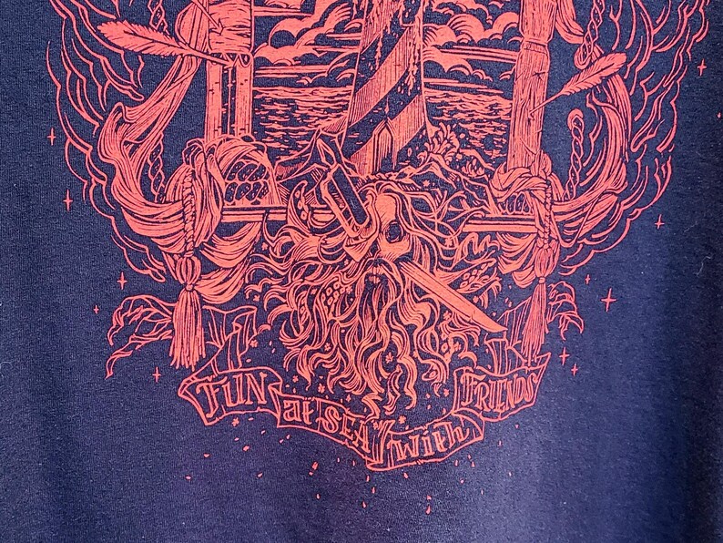 A closeup of the bottom of the red pirate shirt shows a pirate skull with a sword through it's eye and the text: fun at sea with friends.