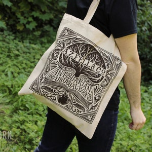 An off-white tote bag with black ink screen printing is worn over a model's shoulder. The text of the design reads AZ FEL & CO. Antiquarian and Unusual Books.