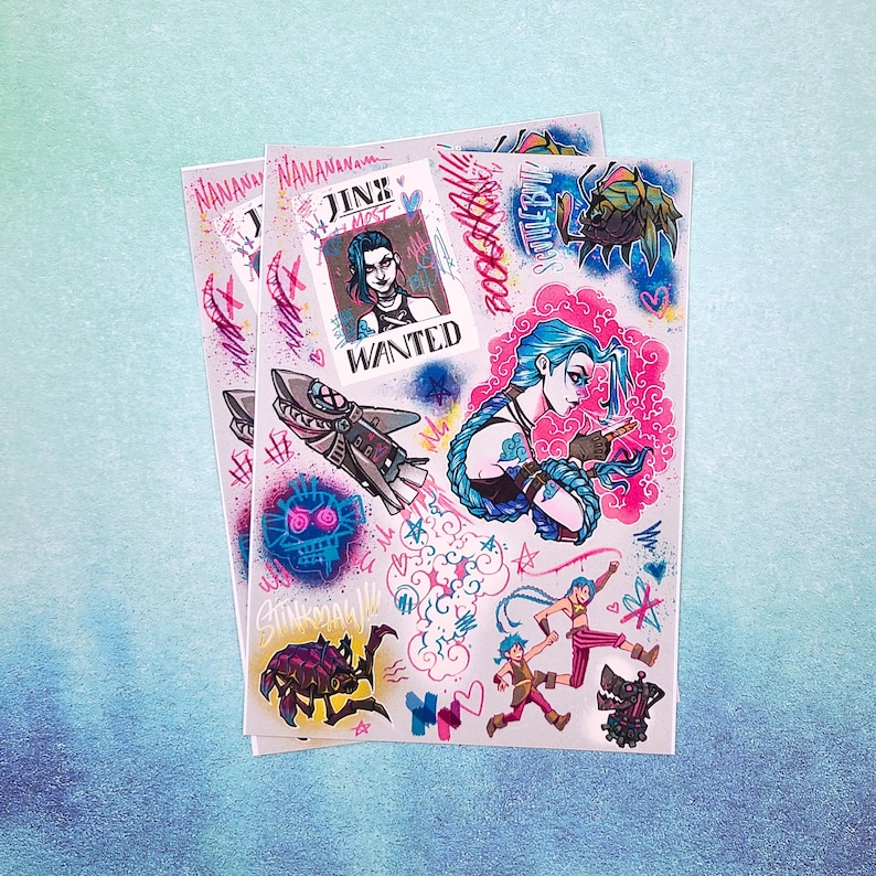 May include: A set of colorful stickers featuring characters from the video game League of Legends. The stickers feature Jinx, Vi, and Powder, with the text "Jinx Most Wanted" and other graffiti-style designs.