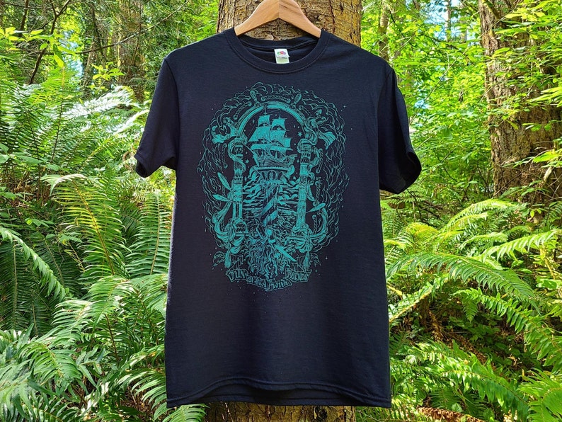 An illustration of the theme gentleman pirates is screen printed in teal blue ink on a black t-shirt. The illustrated typography on the bottom of the shirt reads fun with friends at sea.