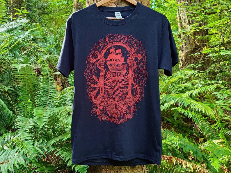 An illustration of the theme gentleman pirates is screen printed in bright red ink on a black t-shirt. The illustrated typography on the bottom of the shirt reads fun with friends at sea.