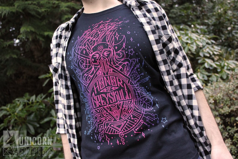 Puede incluir: Camiseta negra con un dise&ntilde;o gr&aacute;fico rosa y azul ne&oacute;n que incluye el texto "Honor of Greyskull". La camiseta se usa con una camisa a cuadros en blanco y negro.