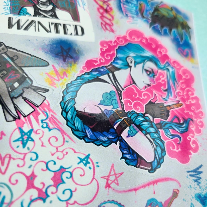 May include: A sticker sheet featuring a colorful illustration of a female character with blue hair and a pink background. The character is holding a gun and has a cloud-like design on her arm. The sticker sheet also includes a rocket, stars, and the word "WANTED".