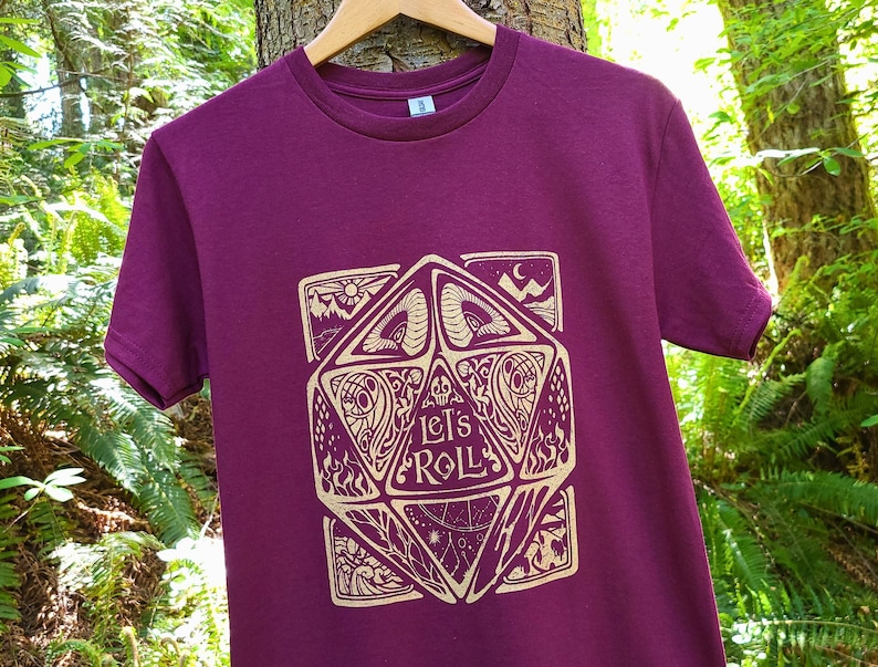 May include: Burgundy t-shirt featuring a gold graphic of a dice with the words "Let's Roll" on it.