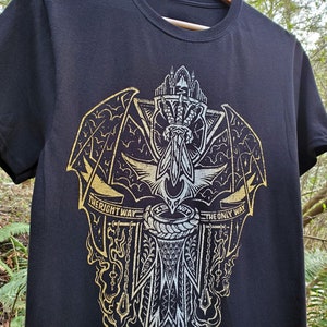 Peut inclure: T-shirt noir avec un imprim&eacute; graphique or et blanc d'une cr&eacute;ature ail&eacute;e avec une &eacute;p&eacute;e. Le graphique comprend le texte "The right way is not the only way".