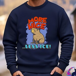 May include: Navy blue sweatshirt featuring a cartoon capybara with the text "MORE NICE ..LESS ICE!" in orange, blue, and teal. The capybara is brown and tan, set against a blue background.