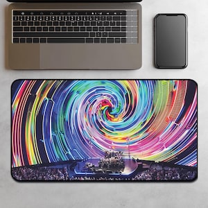 May include: A rectangular mousepad featuring a vibrant, colorful design of a concert stage with a swirling, psychedelic light show. The stage is filled with musicians and a large crowd. A laptop and smartphone are visible.