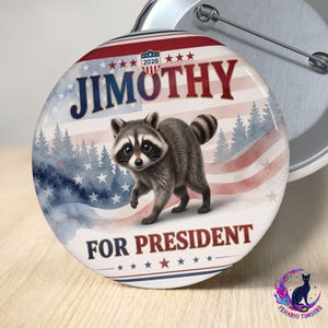 Op de afbeelding: Een ronde button met een aquarelillustratie van een wasbeer tegen een achtergrond van de Amerikaanse vlag en dennenbomen. De tekst luidt JIMOTHY bovenaan en FOR PRESIDENT onderaan, met 2028 in een klein schildje in het midden weergegeven.
