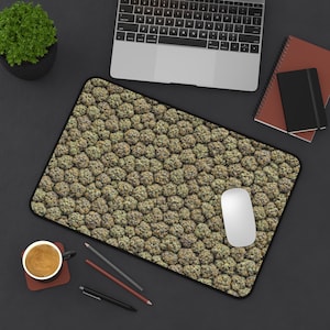 May include: A rectangular mousepad with a repeating pattern of green and brown buds. A white computer mouse sits on the pad, with a laptop, notebooks, pens, and a cup of coffee nearby.